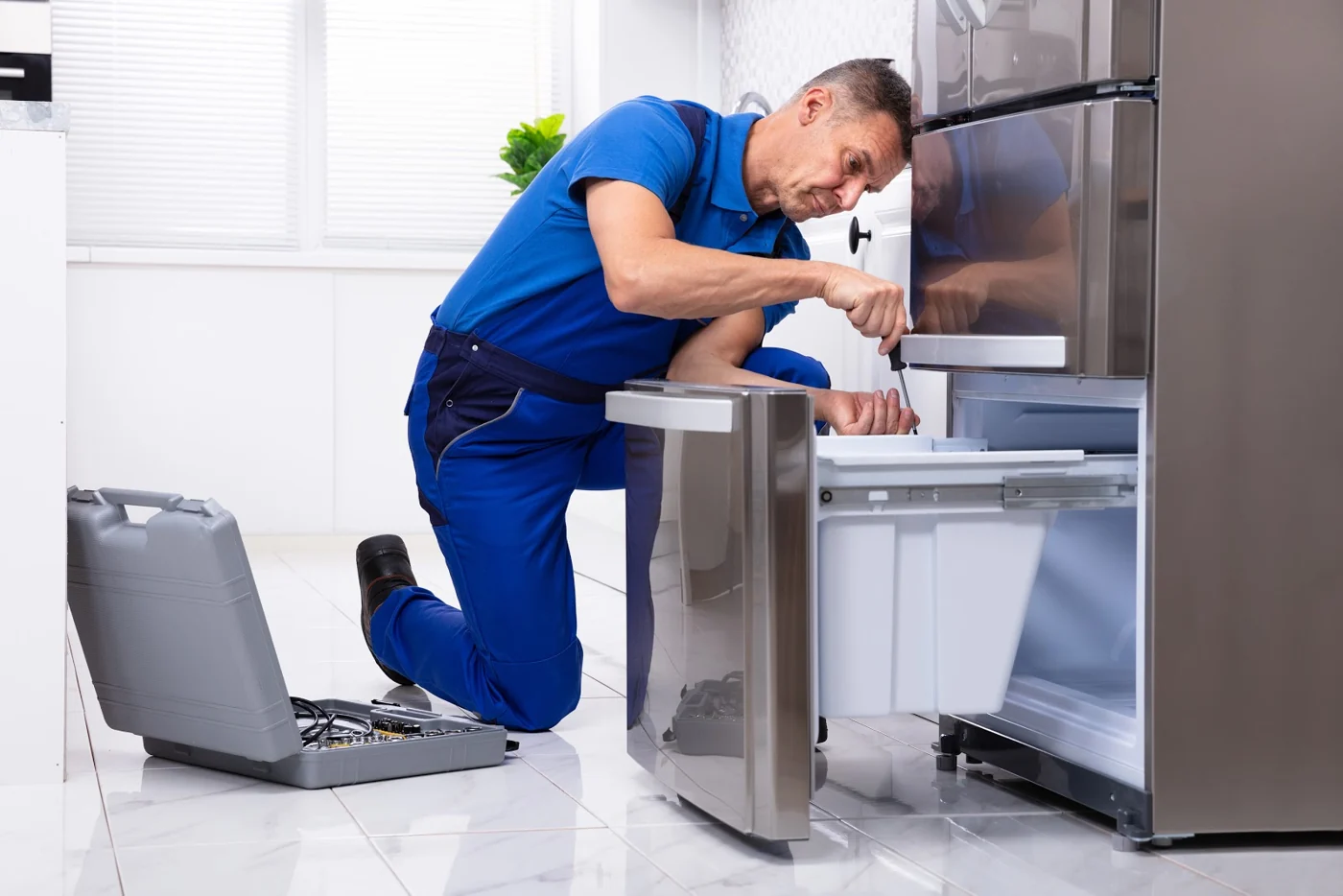 Technician adjusting a refrigerator drawer with a screwdriver in a home kitchen